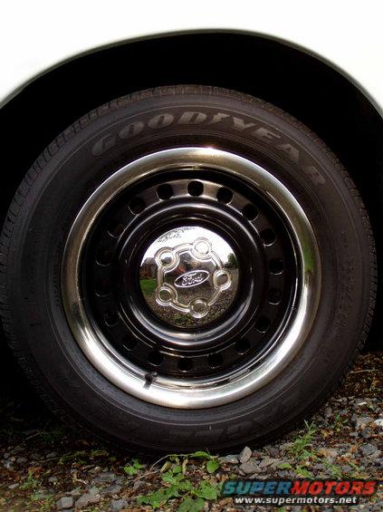 Close-up of a black steel wheel with a chrome trim ring and a Ford-branded hubcap. Goodyear tire visible