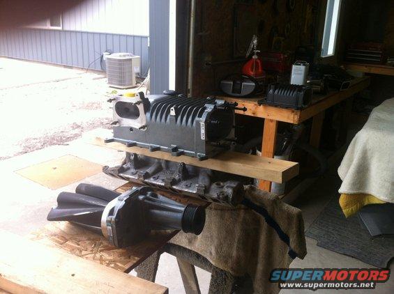 Supercharger and engine block on sawhorses in a garage. Supermotors.net logo visible