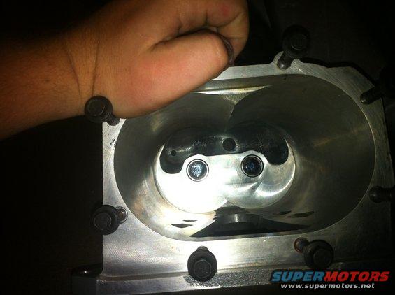Close-up of supercharger rotors with a hand obscuring part of the intake. Metal casing with bolts visible