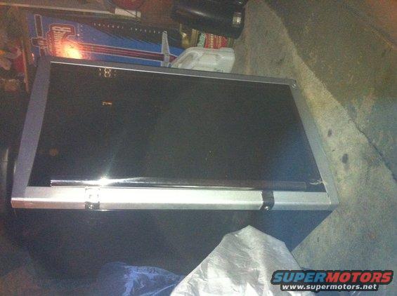 Black tool chest with silver trim, sitting on a concrete floor. Some blue and red graphics are visible in the background