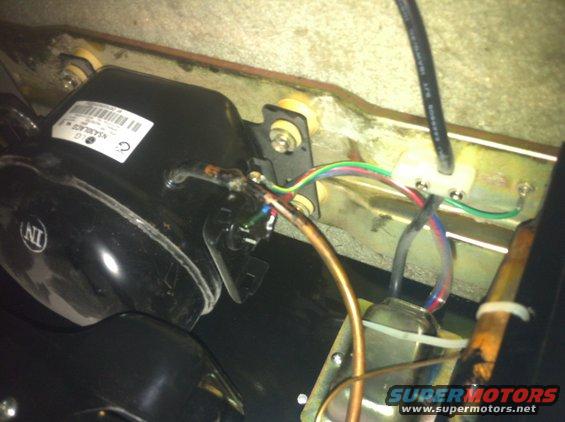 Black compressor with a white label and colorful wires attached to a metal bracket