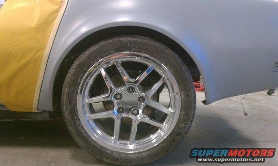 Close-up of a car's rear wheel and fender, with yellow masking tape on the body panel