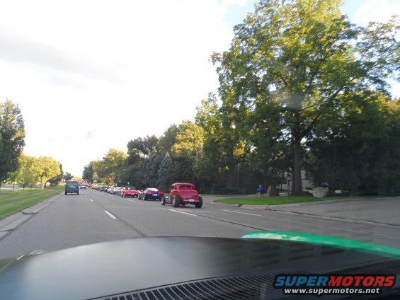 Red hot rod in a line of cars on a tree-lined road