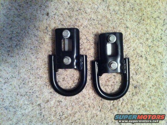 Two black metal tow hooks with D-rings, bolted to a carpeted surface