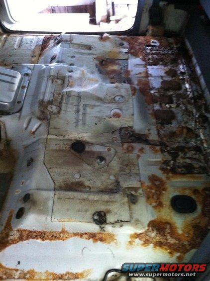 Rusted interior floor pan with visible mounting points and rubber grommets