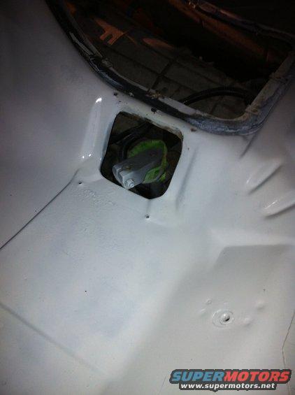 Close-up of a vehicle's white painted floor with a hole revealing some green and gray mechanical parts underneath