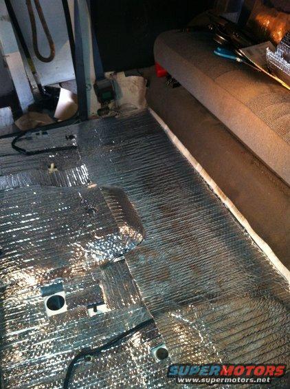Sound deadening material installed on the floor of a vehicle interior, with a portion of a seat visible