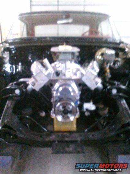 Engine bay with a chrome V8 engine, intake manifold, and carburetor. The car's interior and windshield are visible