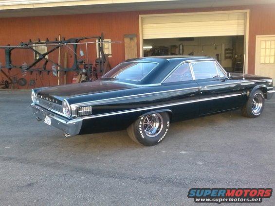 Black coupe with chrome trim and custom wheels parked in front of a garage