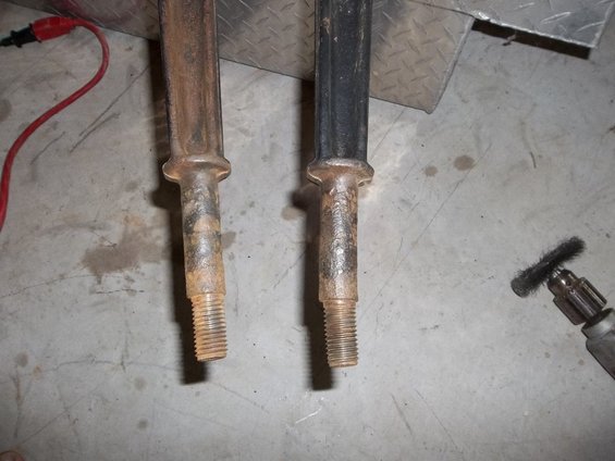 Two metal shafts, one rusty and one black, with threaded ends and a wire brush tool nearby