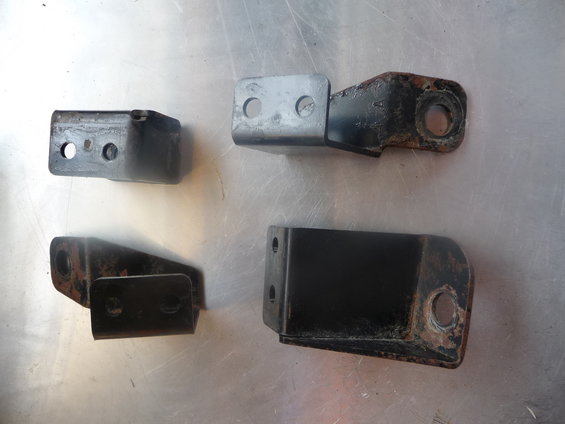 Four metal brackets, some rusted, on a metal surface