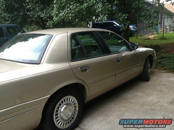 Gold Ford Crown Victoria parked in a driveway. Another car is visible in the background