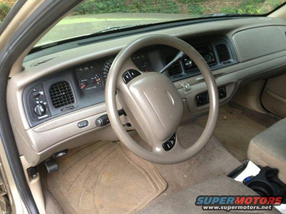Tan car interior with a beige steering wheel and dashboard. Visible dashboard gauges and air vents