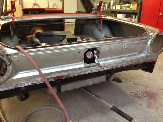 Car's rear end is stripped down to metal, showing the trunk area and fuel filler. A hose is nearby