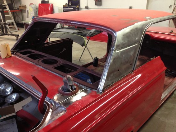 Red 1964 Ford Fairlane interior with removed dashboard and roof panel, showing metal bodywork and some parts in a workshop