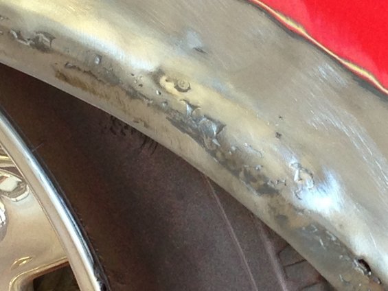 Close-up of a red car's wheel well and fender edge with visible bodywork imperfections