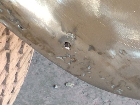Close-up of a damaged metal panel with rust spots and a small square hole