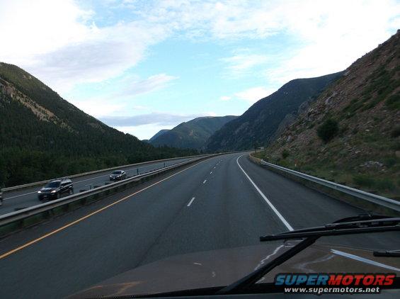 View from a vehicle driving on a highway through a mountainous area, with other cars on the road