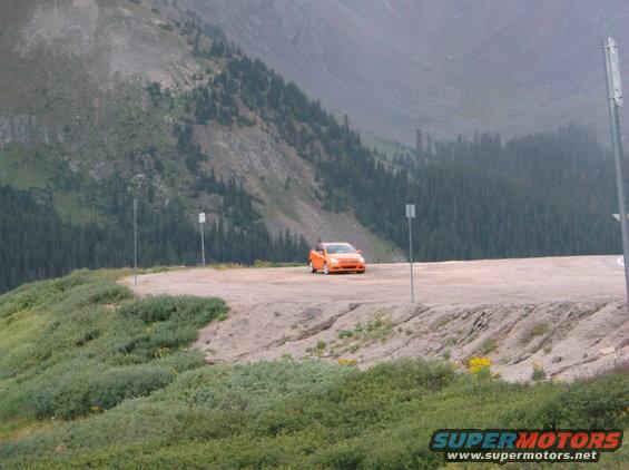 Orange hatchback parked on a dirt road with mountains in the background