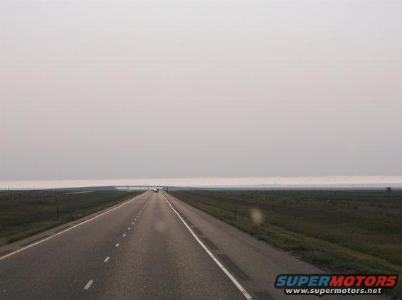 long highway stretching into hazy distance with a few cars far ahead