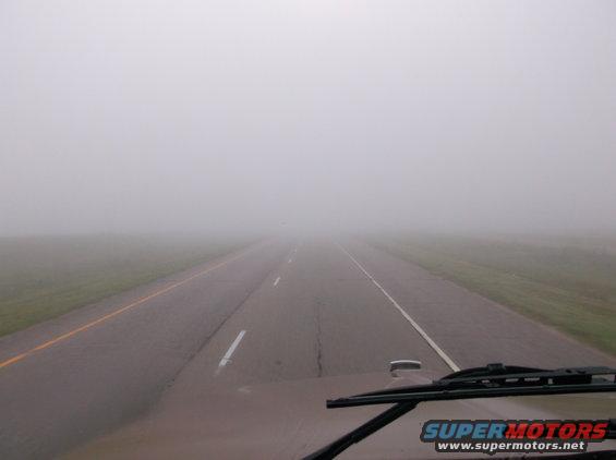 Truck dashboard and windshield view of a highway disappearing into thick fog