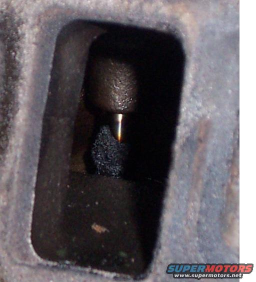 Close-up of a dark engine part with a metal rod and black debris inside a rectangular opening