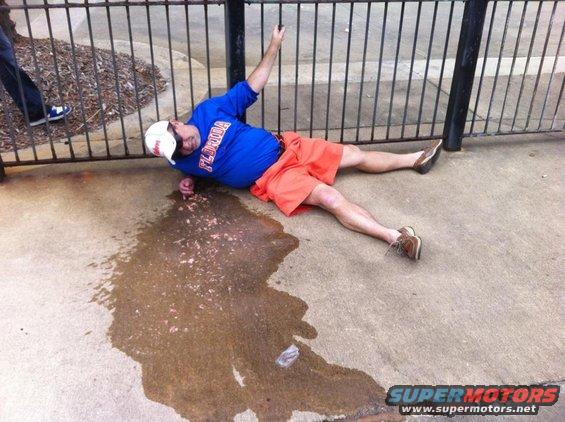 Man in blue shirt and orange shorts on ground near fence