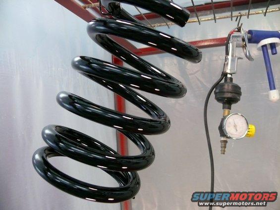 Black coil spring hanging from rack with spray gun and pressure gauge