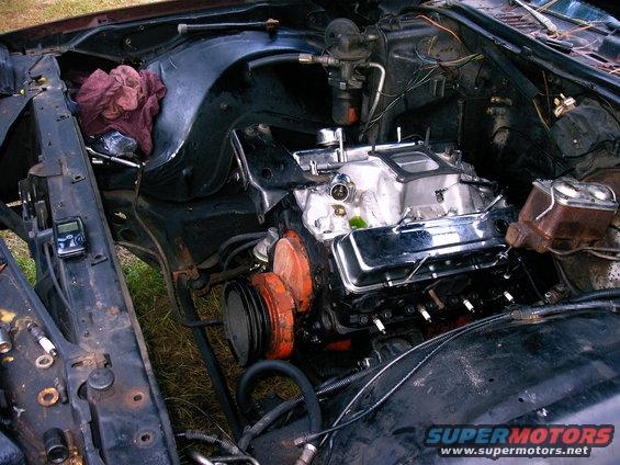 Engine bay with V8 engine, chrome valve covers, and orange pulleys. A digital device is attached to the fender
