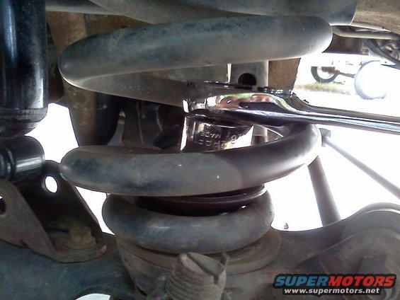 Close-up of a suspension coil spring with a wrench on it. Text on the wrench is partially visible