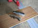 2005 Ford Excursion - Two bumper parts, one chrome and one black, lie on a wooden board next to a red chainsaw.