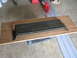 2005 Ford Excursion - A black plastic part, possibly from a vehicle's undercarriage, rests on a piece of plywood.