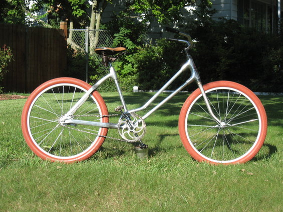 Silver bicycle with orange tires and a brown leather seat, viewed from the side