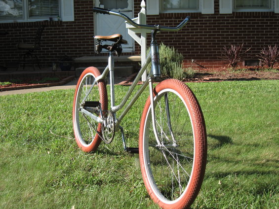 Silver bicycle with orange tires parked on a grassy lawn in front of a brick house
