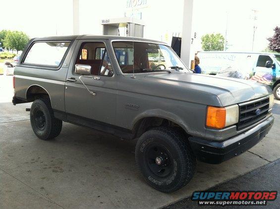 Gray 1987 Ford Bronco parked at a gas station with a white van in the background