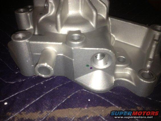 Close-up of a silver metal automotive part with several ports and bolt holes. It sits on a dark, quilted fabric