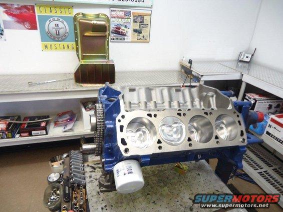 Blue engine block with pistons visible, oil filter attached, on a workbench