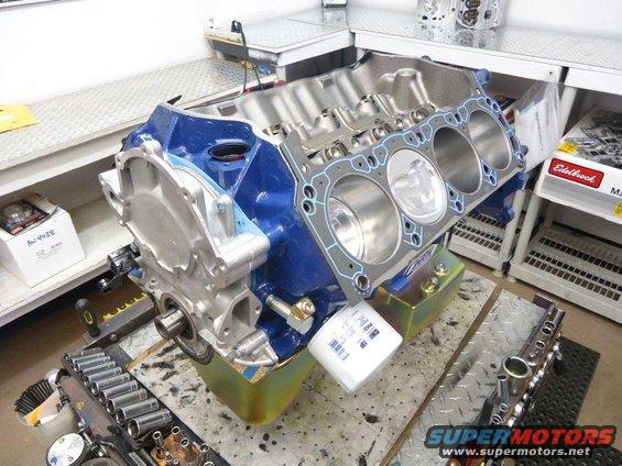 Blue engine block with pistons, gasket, and oil filter on workbench