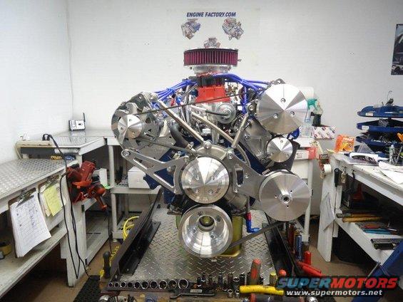 custom V8 engine with chrome pulleys and blue hoses, on a stand in a workshop