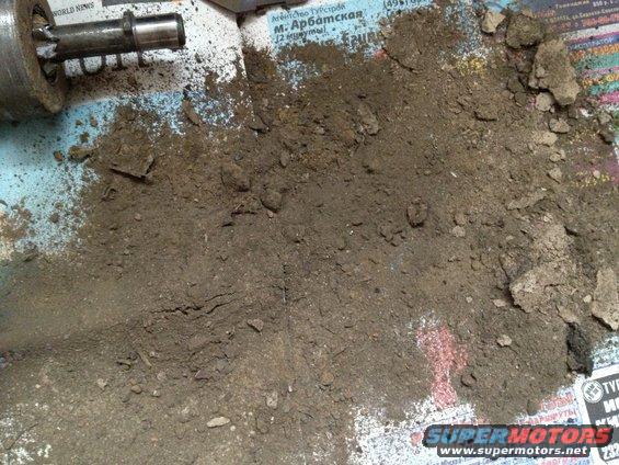Metal starter motor part with dirt spilled on newspaper. Supermotors.net logo visible