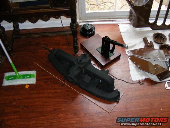 Black engine manifold and various metal parts on a wooden floor