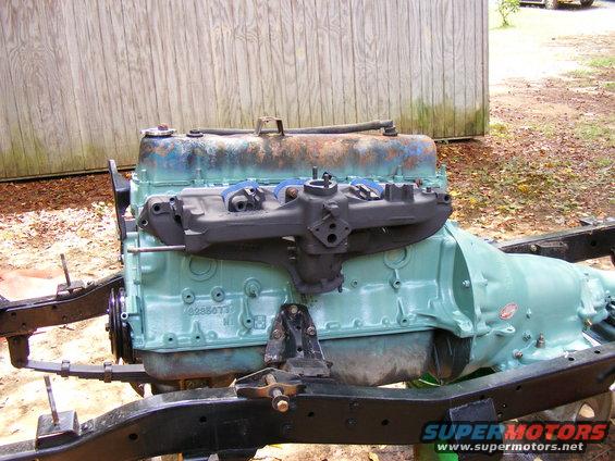 Engine and transmission assembly on a frame. Engine is teal with a black intake manifold. Transmission is also teal