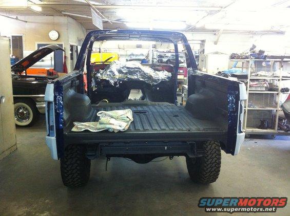 Blue Ford Bronco body stripped down, viewed from the rear in a workshop