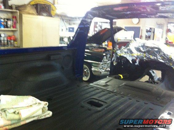 Interior of blue pickup truck bed; classic car with chrome grille in background