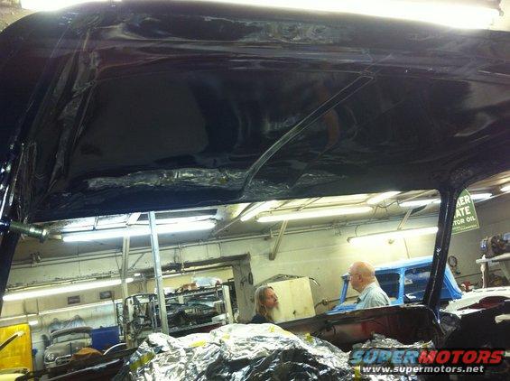 Car interior with black painted roof, people working in shop, another car in background