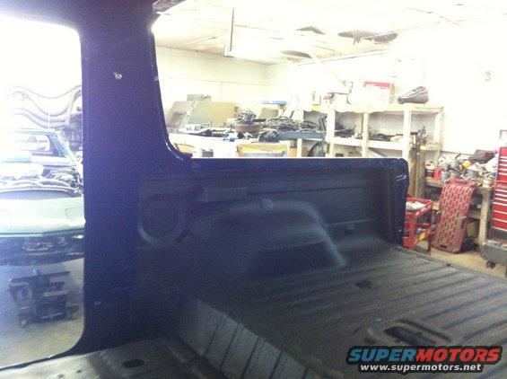 Interior of a dark blue pickup truck bed and cab, with another vehicle visible in the background
