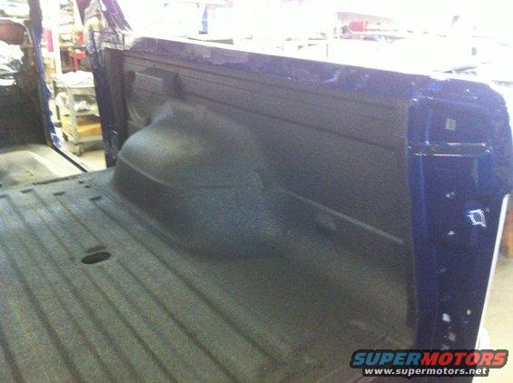 Blue truck bed with spray-in liner. Shows wheel well and tailgate area