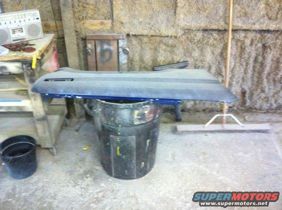 Blue car door panel resting on a trash can in a garage