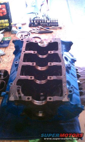 Engine block on a table with tools nearby. Supermotors.net logo visible