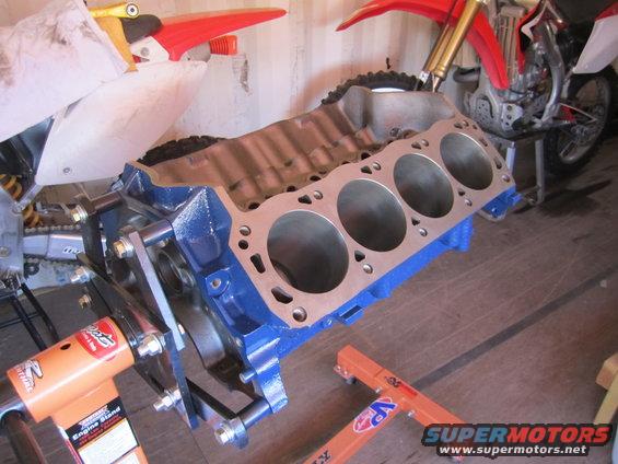 Blue engine block on an orange engine stand, with motorcycles in the background